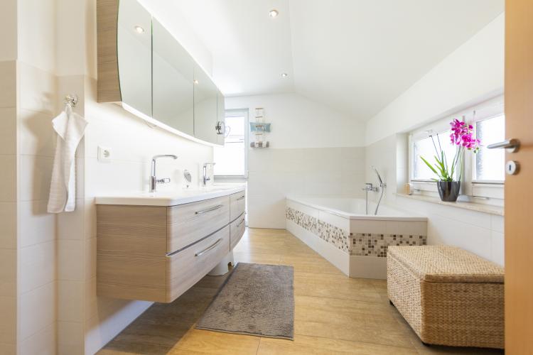 Elegante Linienführung bestimmen das große, in hellen Ocker- und Holzfarben gestaltete Badezimmer mit Wanne und Duschbad. <i>Foto: HELMA Eigenheimbau AG/Christoph Große</i>