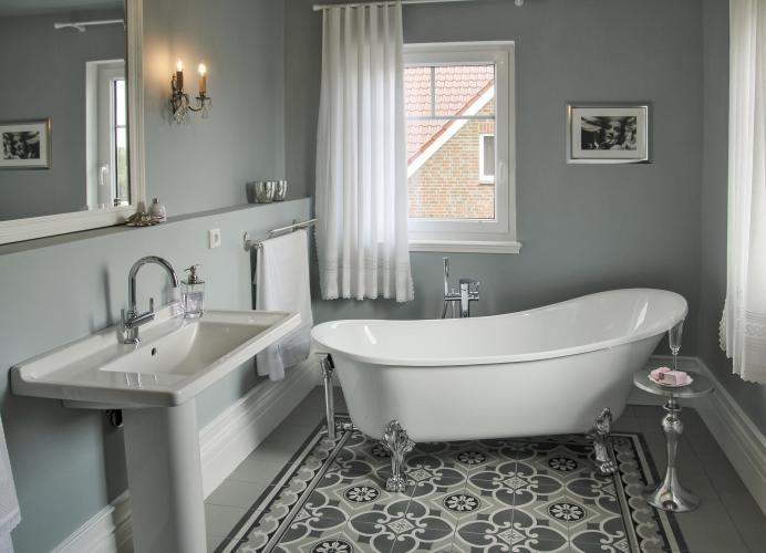 Das Badezimmer in verschiedenen Grautönen setzt mit großflächigen Mustern Akzente. Die freistehende Badewanne und das Waschbecken unterstreichen die Vintage-Optik. <i>Foto: HELMA Eigenheimbau AG</i>