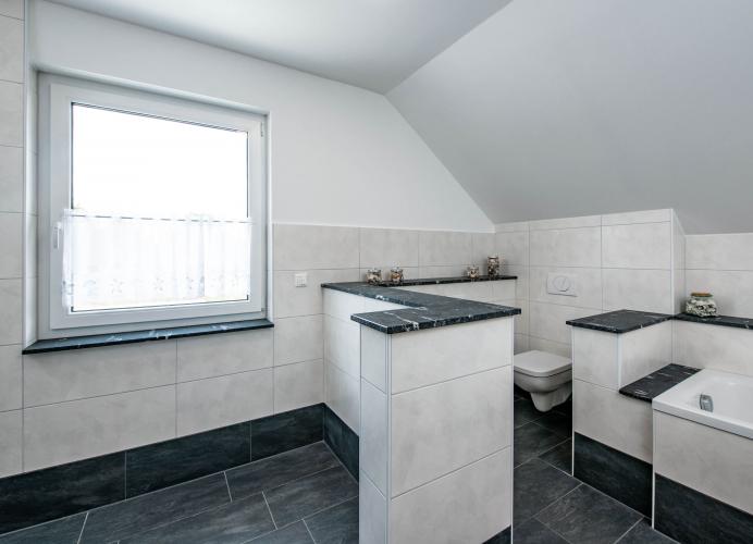 Der Weiß-Anthrazit-Kontrast der Fassade setzt sich im hochwertig ausgestatteten Badezimmer fort. Foto: Helma Eigenheimbau AG / Claudius Pflug