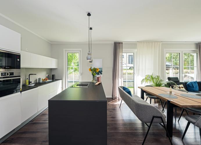 Die integrierte Küche mit Möbelfronten in Weiß und dunklem Anthrazit setzt modern-funktionale Akzente.<i> Foto: Roth-Massivhaus / G. Zwickert</i><br>
